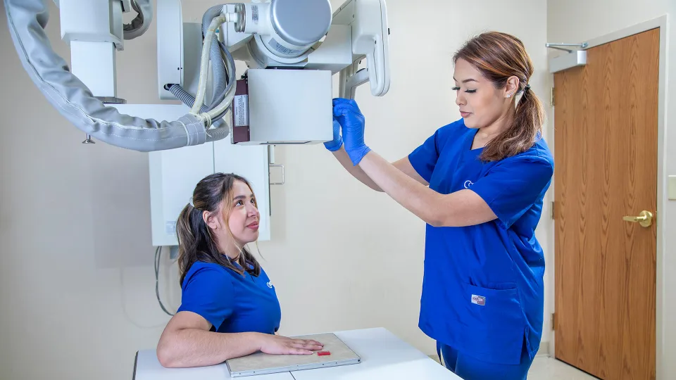A radiology tech adjusts an x-ray machine on a patient's hand.