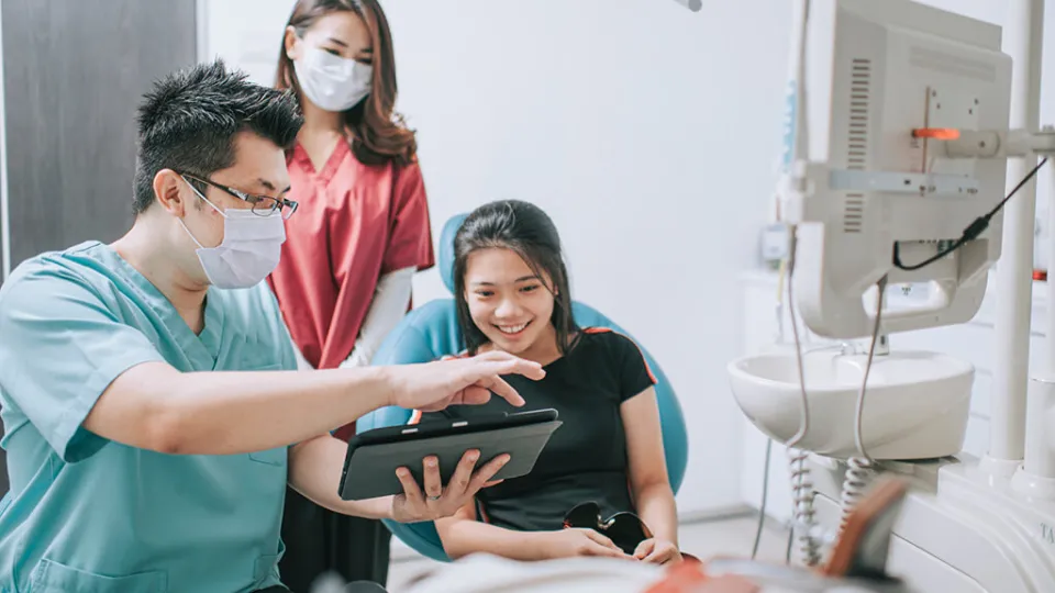 Dental Assistant holds tablet to educate smiling young patient