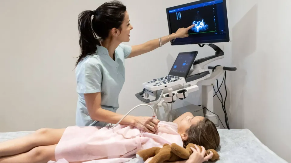 Echocardiogram technician performing heart ultrasound on child and reviewing cardiac images on screen during exam. Echocardiogram technician performing heart ultrasound on child and reviewing cardiac images on screen during exam.