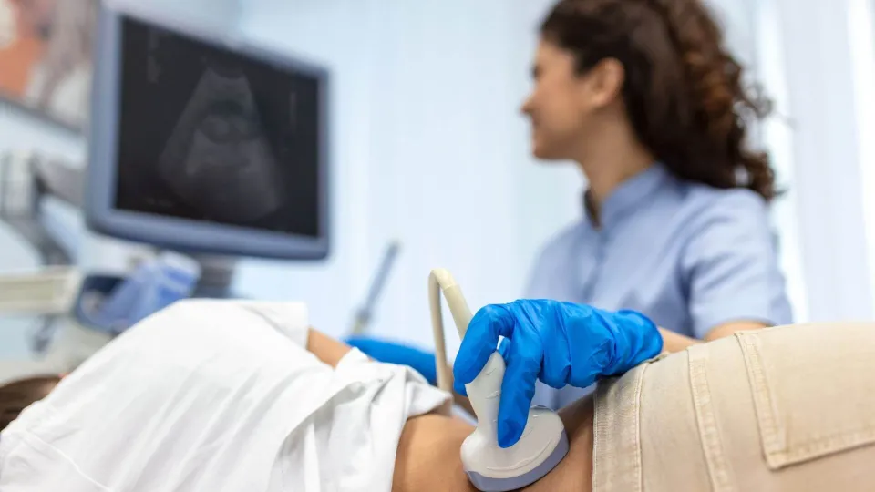 Sonographer conducting abdominal ultrasound with patient while monitoring live scan results. Sonographer conducting abdominal ultrasound with patient while monitoring live scan results.