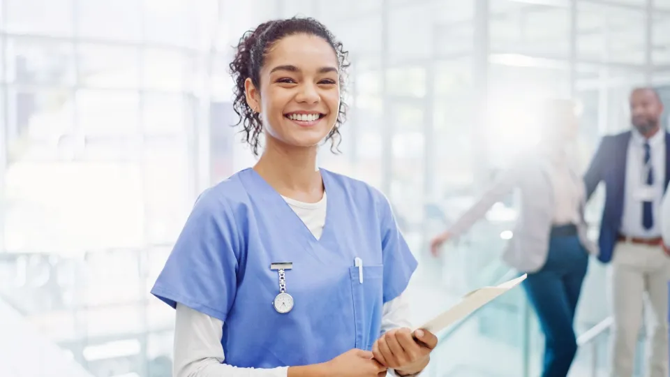 Medical assistant holding a clipboard and smiling in a modern healthcare facility.