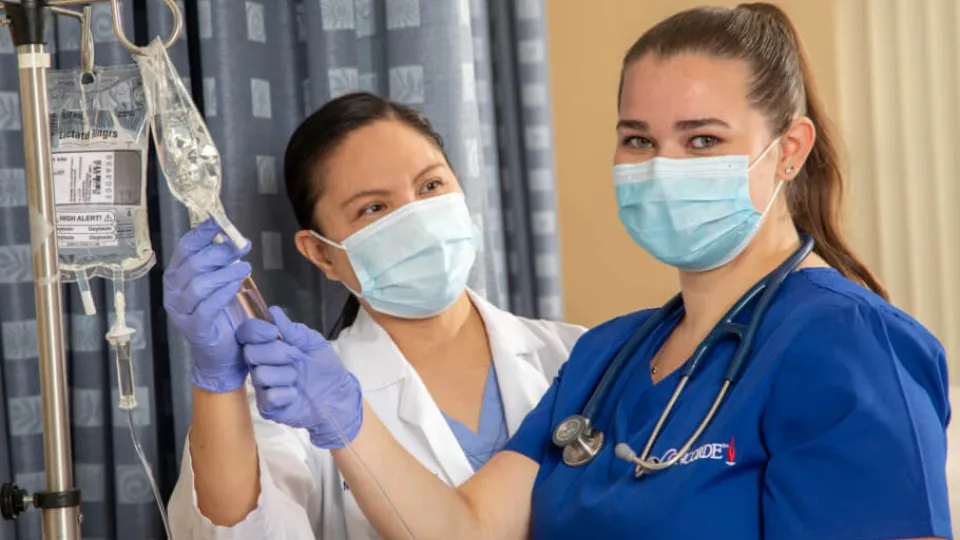 Nursing student learning to check IV fluid levels during hands-on training session Nursing student learning to check IV fluid levels during hands-on training session