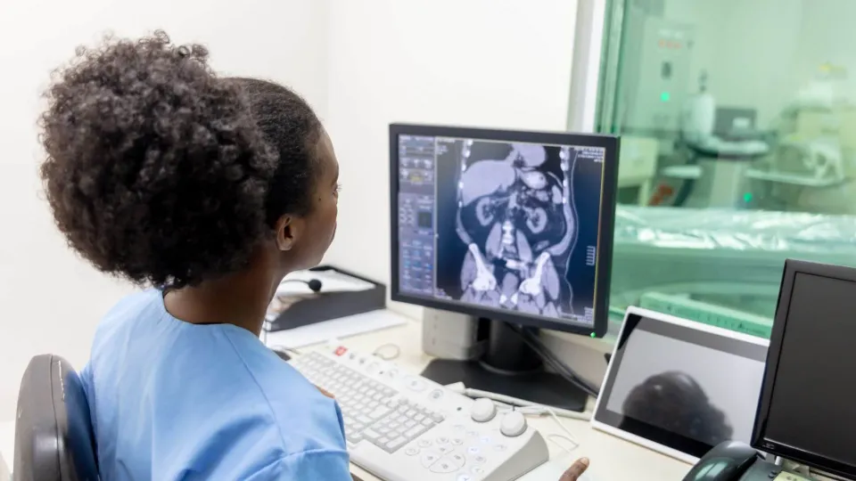 Radiologic technologist analyzing abdominal CT scan on monitor in a medical imaging control room. Radiologic technologist analyzing abdominal CT scan on monitor in a medical imaging control room.