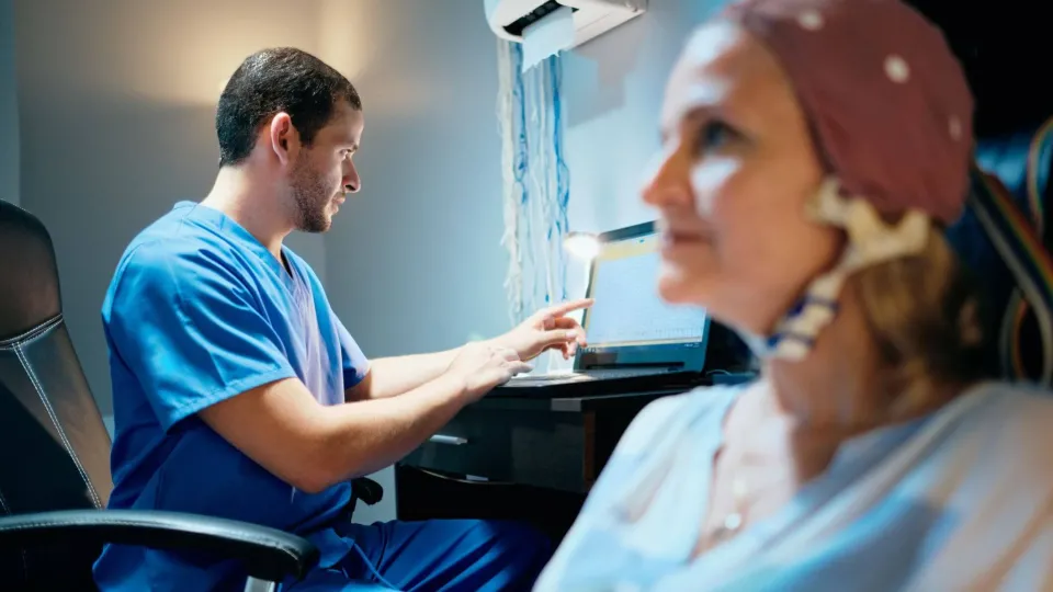 EEG technician monitoring brain wave activity on screen while patient undergoes neurological testing in clinical setting EEG technician monitoring brain wave activity on screen while patient undergoes neurological testing in clinical setting