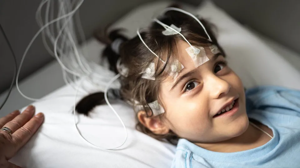 Smiling child with electrodes attached during a sleep study, representing the role of a polysomnographer in monitoring pediatric sleep patterns Smiling child with electrodes attached during a sleep study, representing the role of a polysomnographer in monitoring pediatric sleep patterns