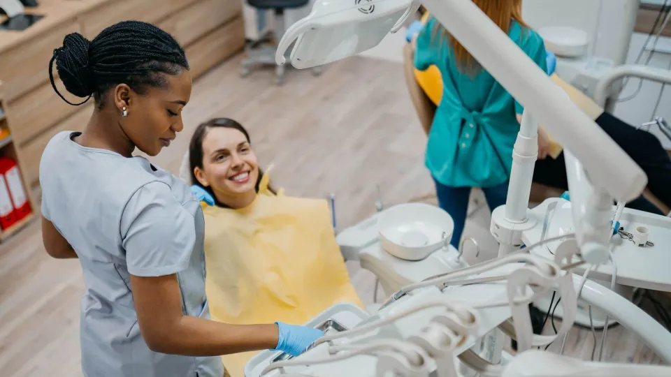 Dental assistant helping a patient in the dental chair during a clinical procedure, reflecting patient care responsibilities in the role. Dental assistant helping a patient in the dental chair during a clinical procedure, reflecting patient care responsibilities in the role.