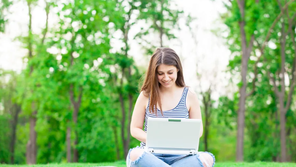 female teenager high school graduate researching on laptop outside during summer