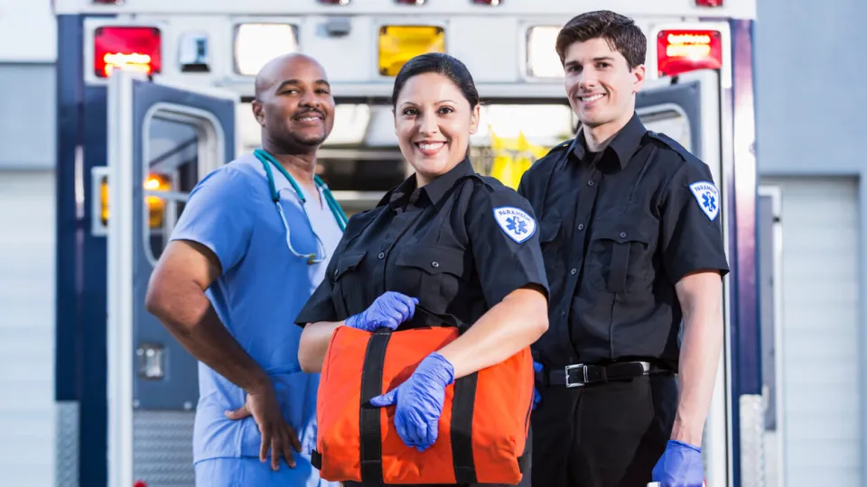 First responders, two paramedics and a healthcare worker, pose in front of and ambulance
