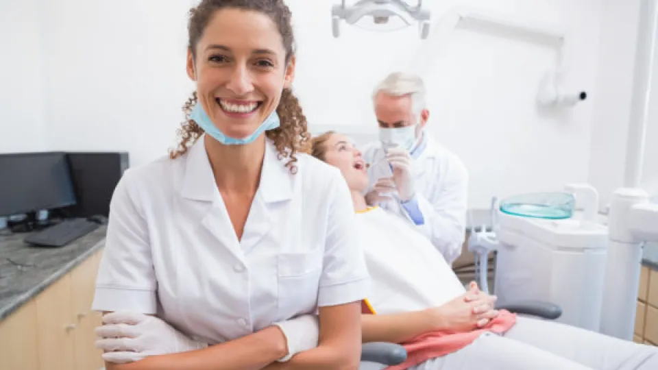 Dental assistant smiling at camera with dentist and patient behind at the dental clinic