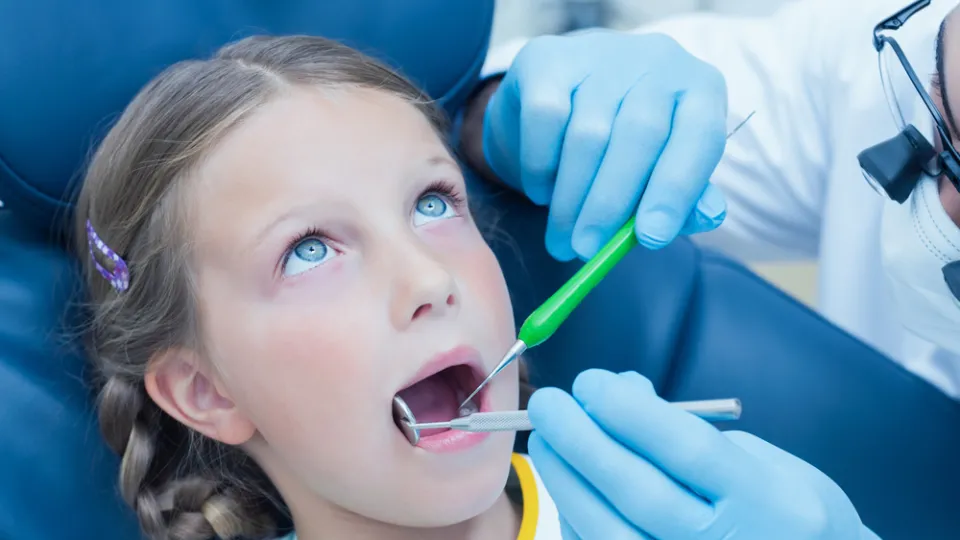 Male dentist examining girls teeth in the dentists chair dental assistant