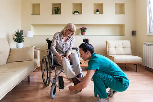 An LVN assists her patient who is in a wheelchair, inside a home