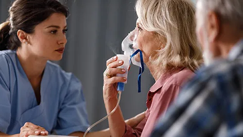 respiratory therapist gives a breathing treatment to older woman