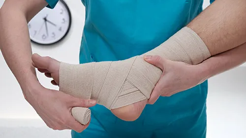 A medical assistant wraps a bandage around a patient's ankle and foot