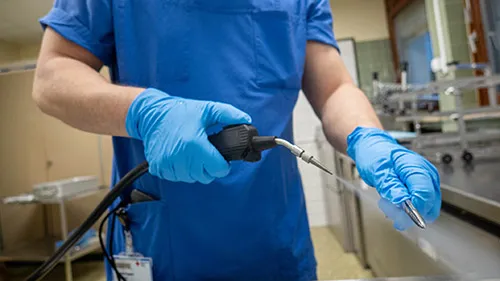 Sterile processing technician pre-cleans a surgical instrument using steam as part of the sterilization process