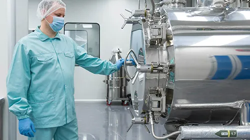 A sterile processing tech wearing full personal protective equipment closes the door on a large autoclave