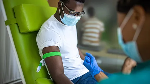 A phlebotomist tightens an elastic band around a patient's right arm to prepare for a blood draw.