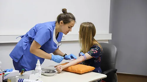 A phlebotomist draws blood from the left arm of her young patient.
