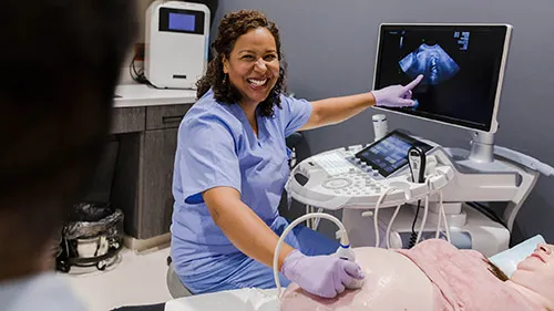 A sonographer smiles and points out a new development of her pregnant patient's fetus.