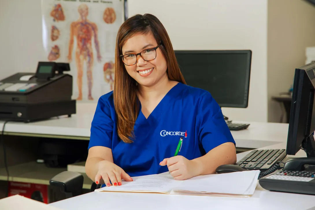 A medical office professional sitting at desk with pen completing paperwork.