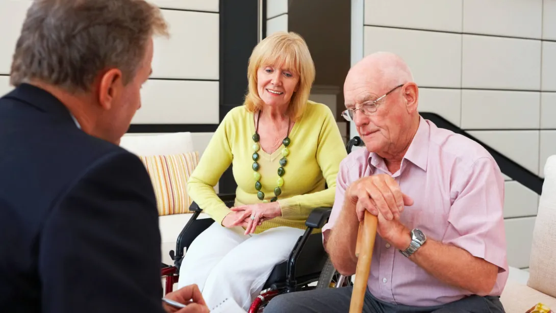 A healthcare administrator speaks with an elderly man and woman about their care experience in the hospital.
